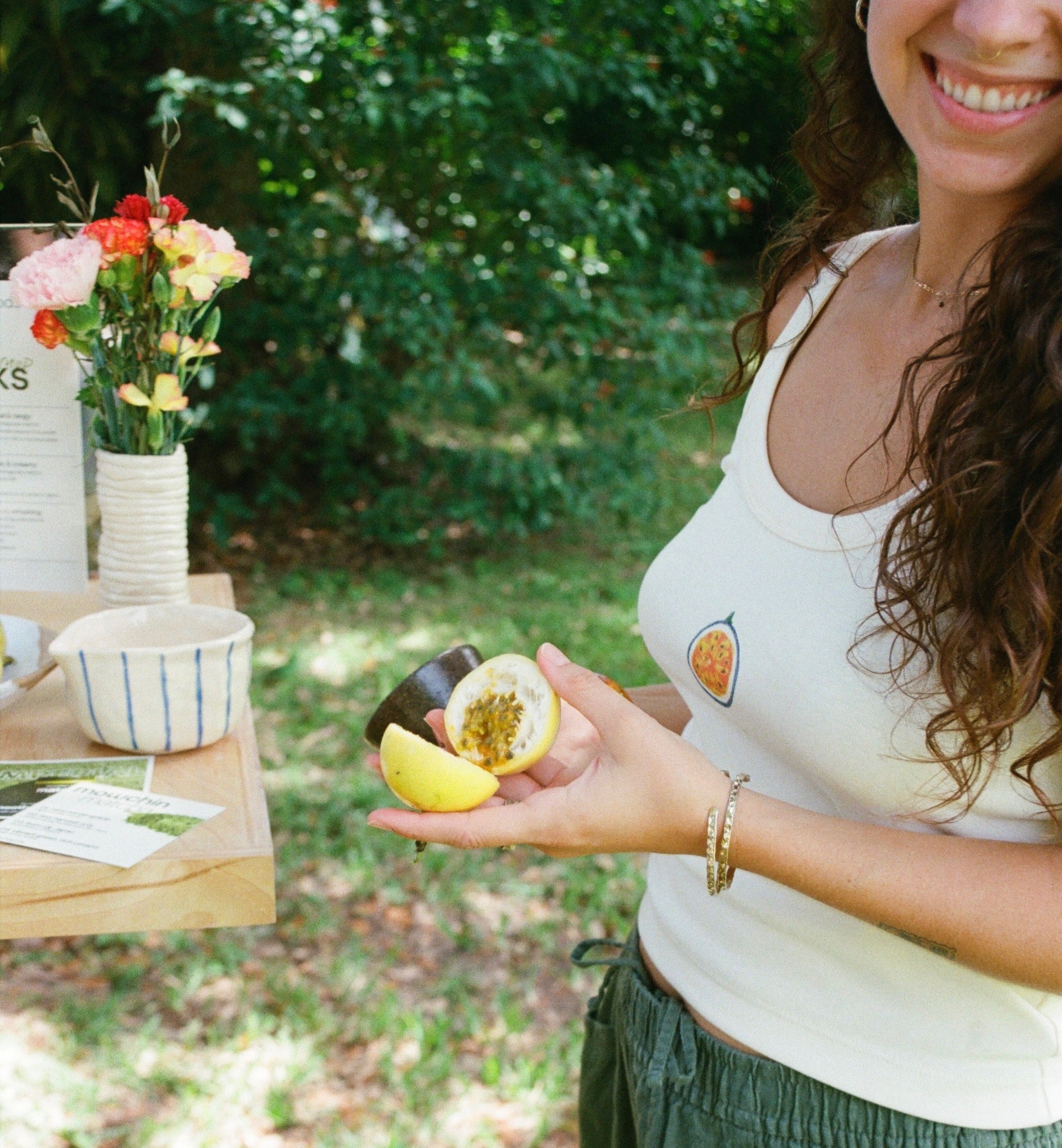 Woman holding a halved fruit outdoors with a blurred background wearing the Ash Tank